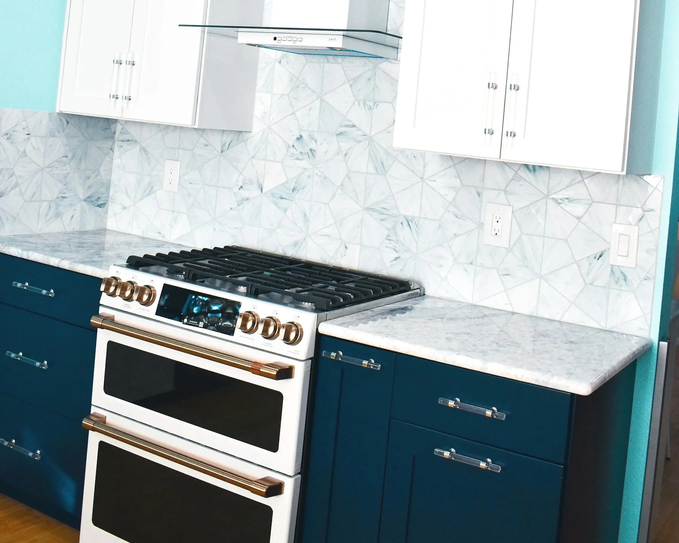 Kitchen with white upper cabinets, blue lower cabinets, a marble backsplash, and a white stove with gold hardware.