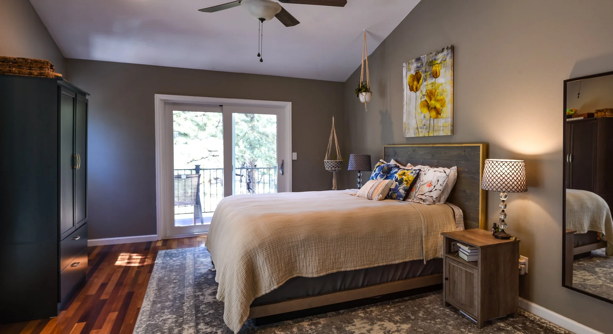 A bedroom with a bed, nightstand, lamps, and sliding glass door leading to a balcony with outdoor furniture.