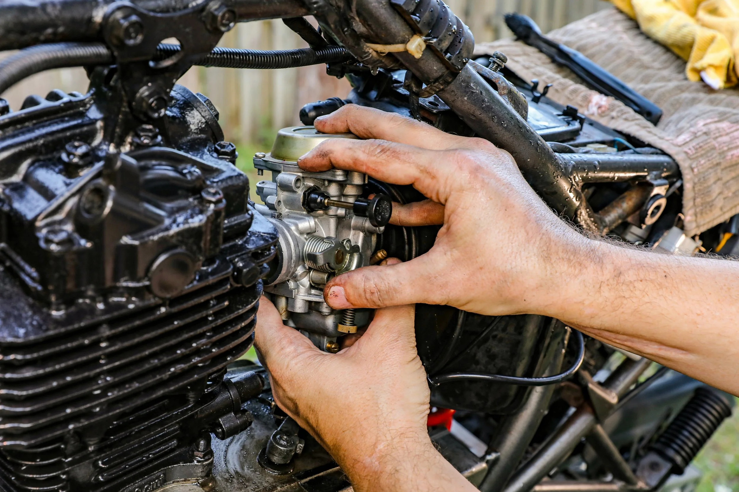 Person's hands working on a motorcycle engine, adjusting or repairing the carburetor.