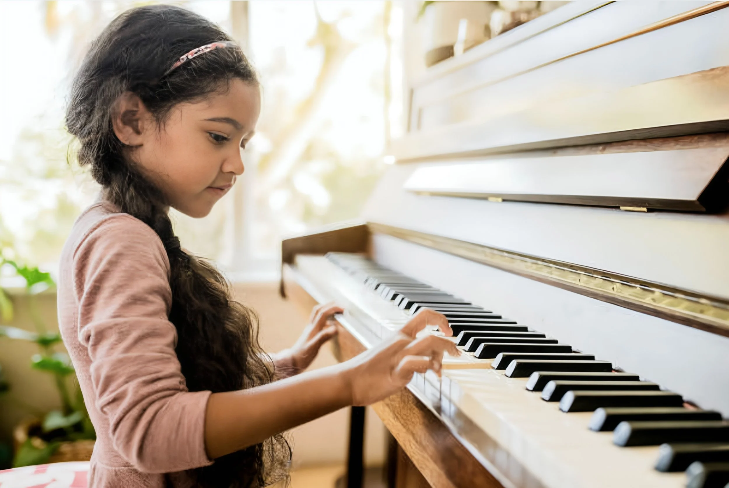 A young girl with long curly hair playing a white upright piano indoors.