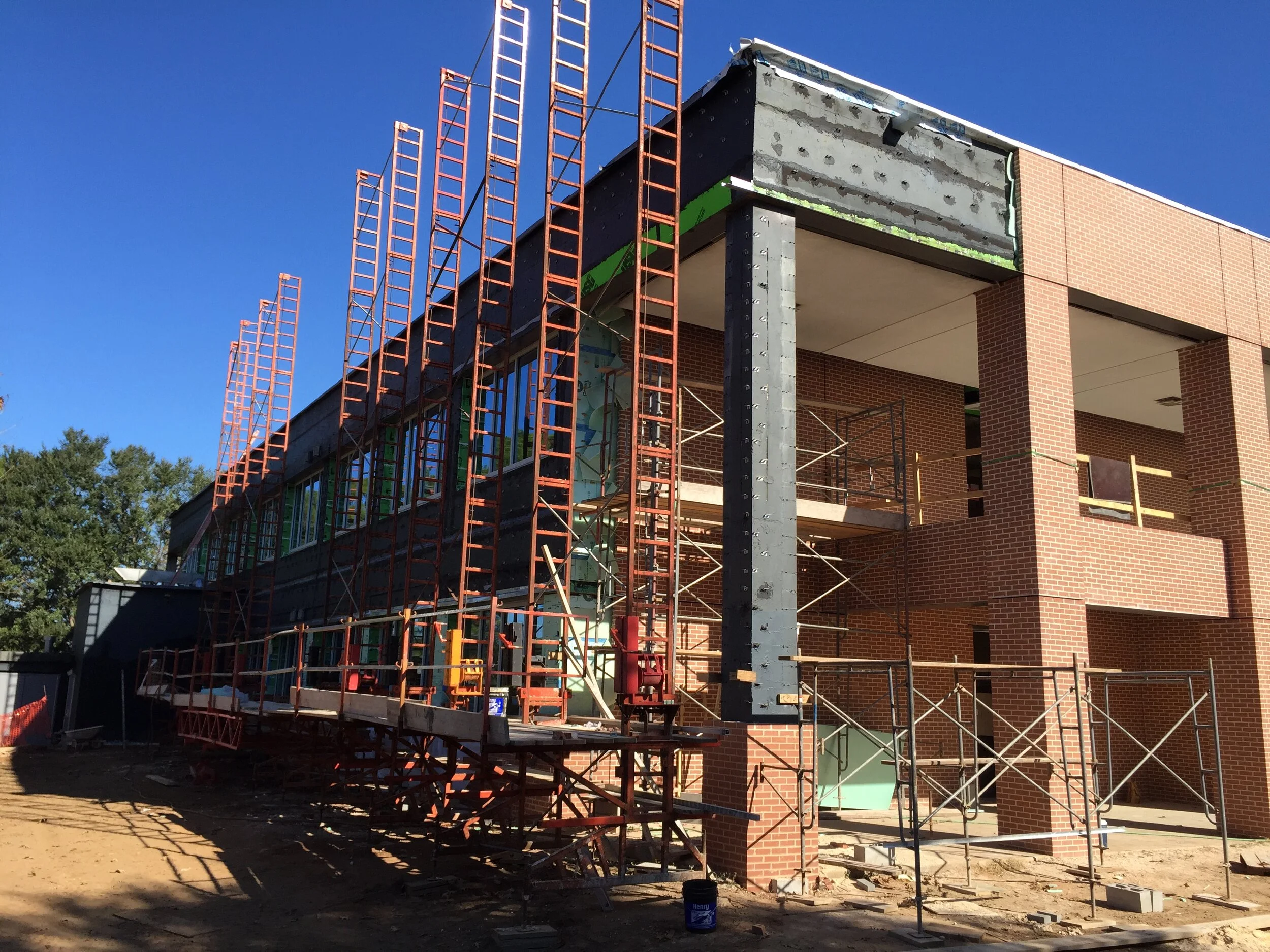 Under construction building with brick exterior, scaffolding, and orange safety ladders, under a clear blue sky.