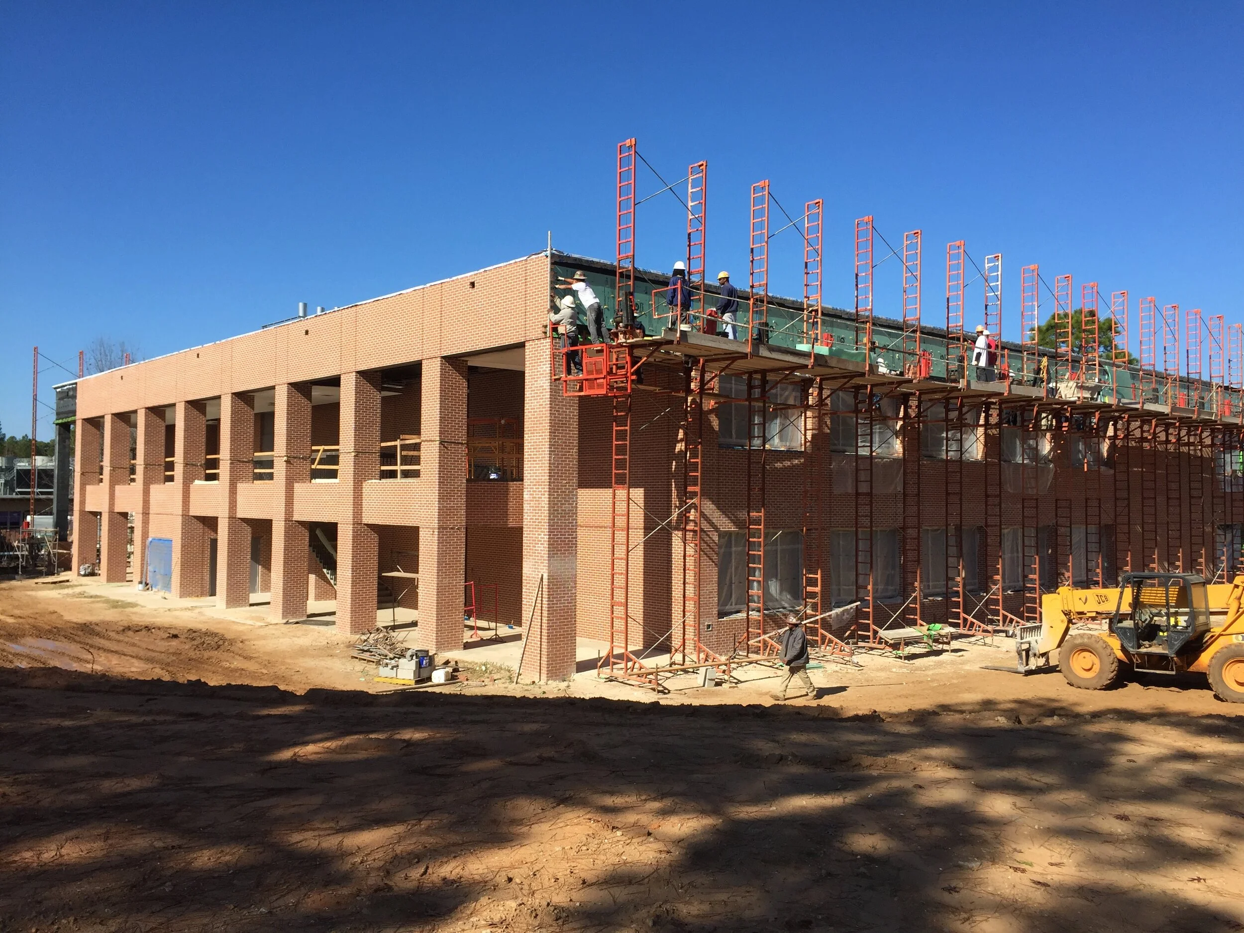 Construction site with workers on scaffolding constructing a multi-story brick building under clear blue sky.