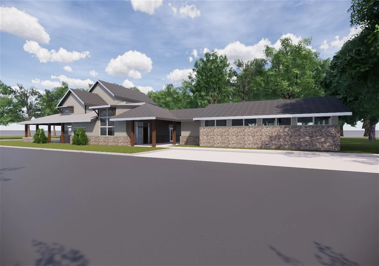 A modern house with gray siding, stone accents, and a dark gray roof, set among trees, with a sidewalk and street in the foreground and a partly cloudy sky above.