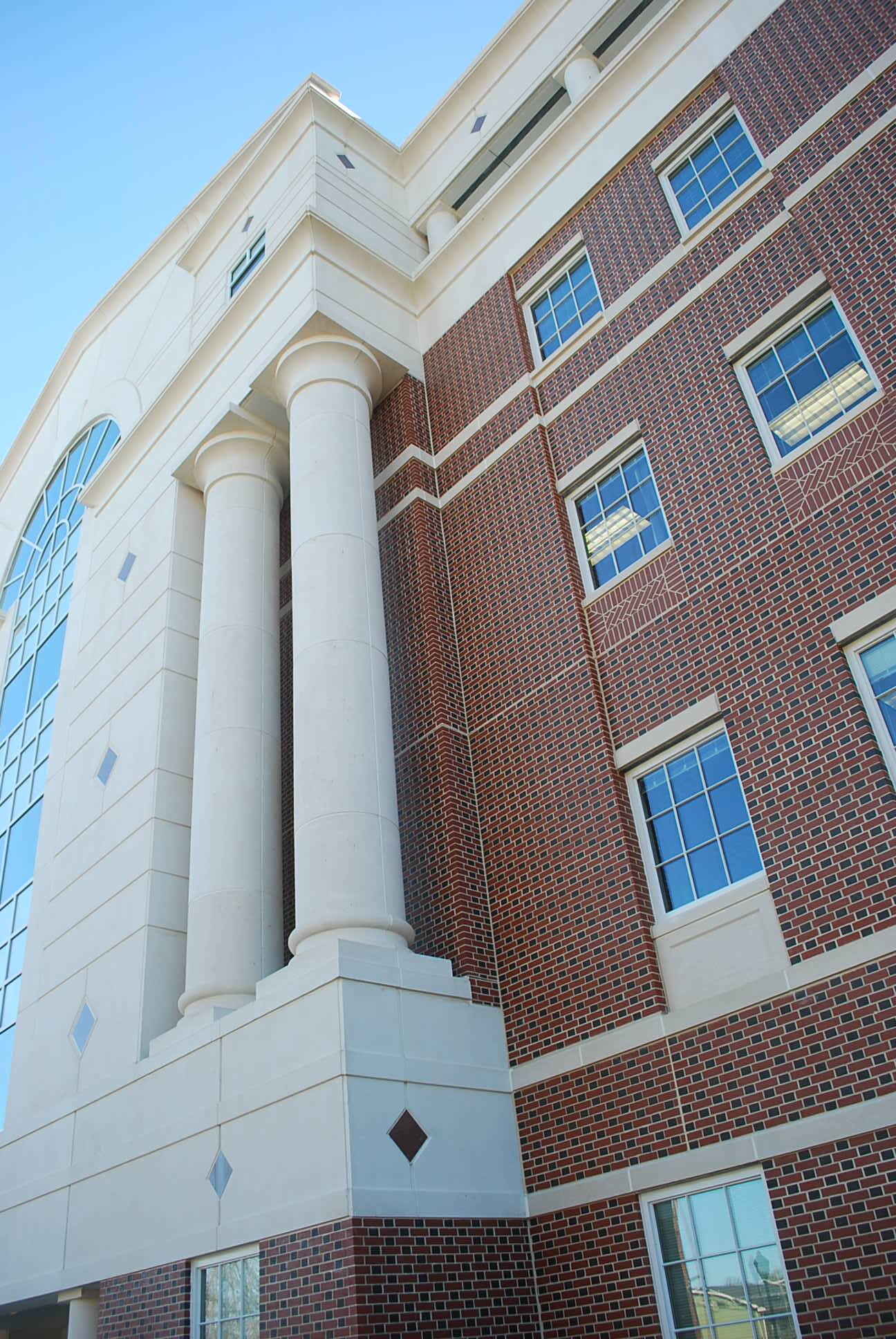 Low-angle view of a building with white columns and red brick exterior, multiple windows, and a clear blue sky in the background.