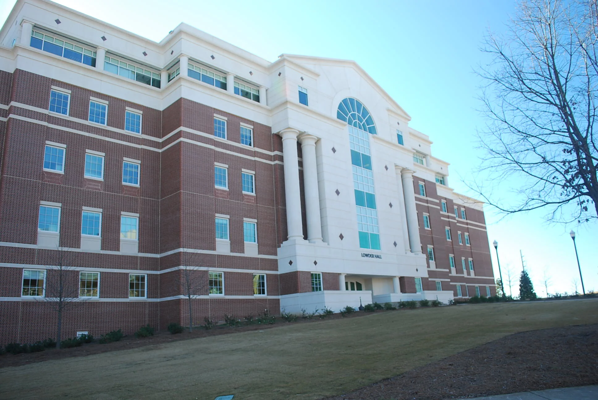 Exterior view of a multi-story brick and white building labeled 'Lower Hall' with large arched window, decorative columns, and a clear blue sky.