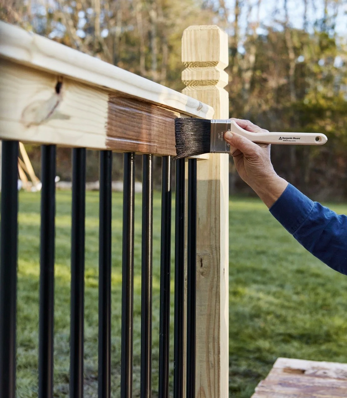 A man brushing Benjamin Moore Woodluxe stain onto a fence outside