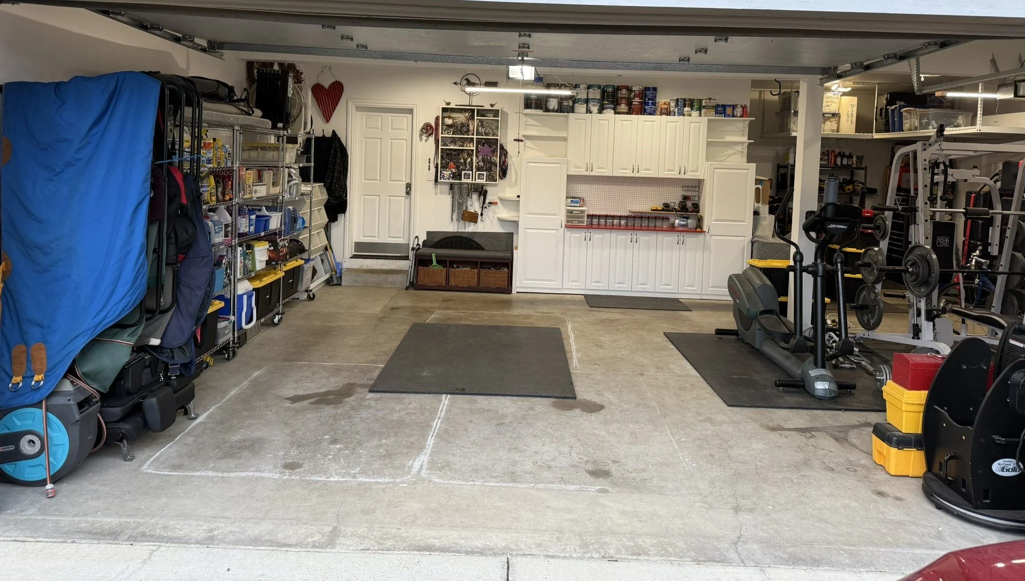 Garage with exercise equipment, storage shelves, and a workbench along the back wall.