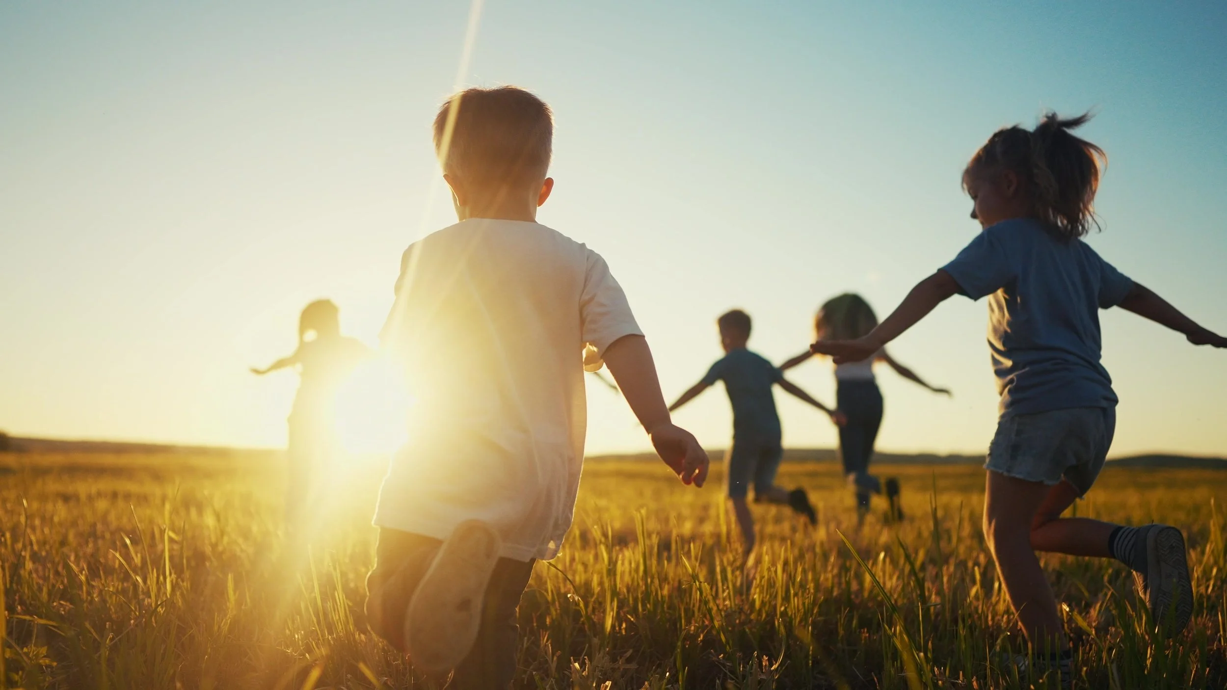 Children playing and running in a field during sunset.
