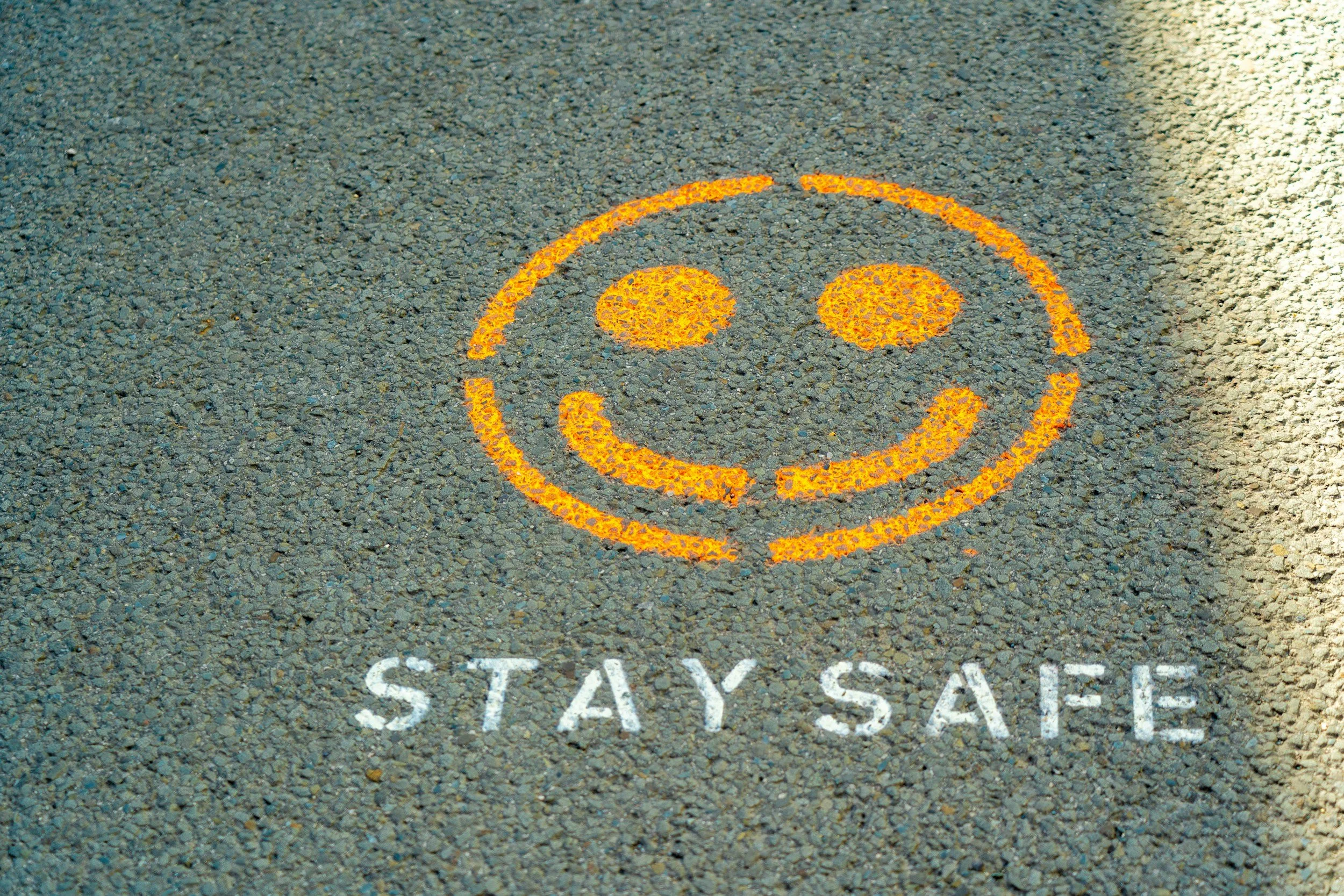 Yellow smiley face and the words "stay safe" painted on asphalt