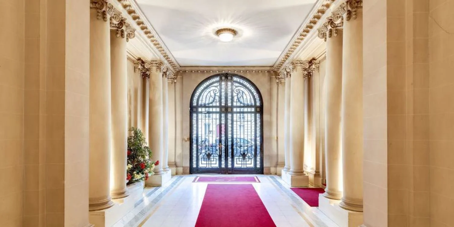 Intérieur d'une entrée avec colonnes ornées, tapis rouge, porte en fer forgé et décoration classique.