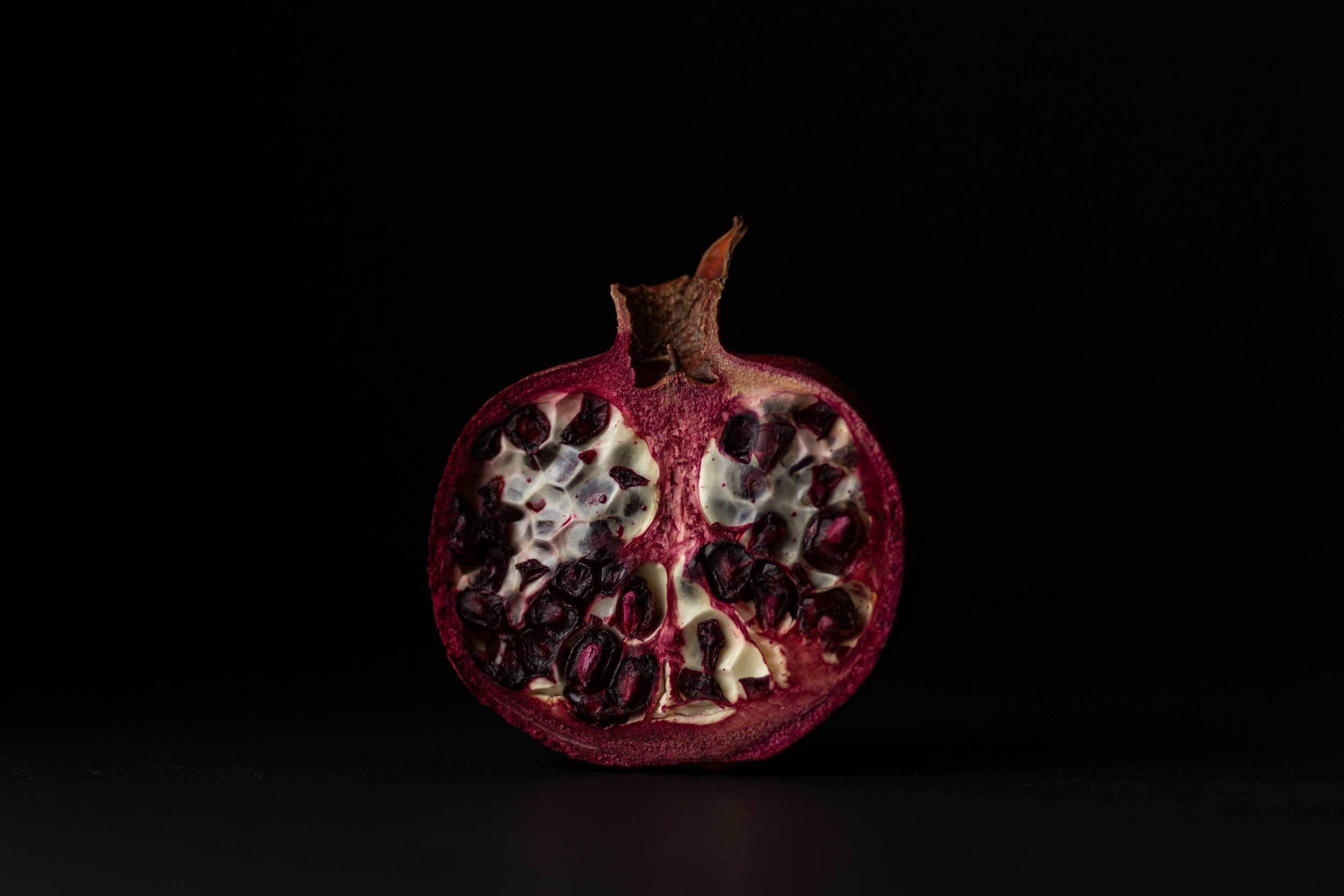 A halved pomegranate fruit with red seeds and white inner membrane against a black background.