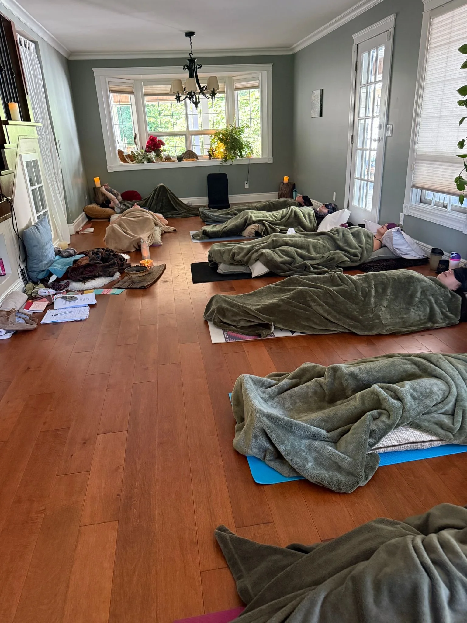 A group of people lying down on yoga mats and blankets in a bright living room during a relaxation or meditation session.
