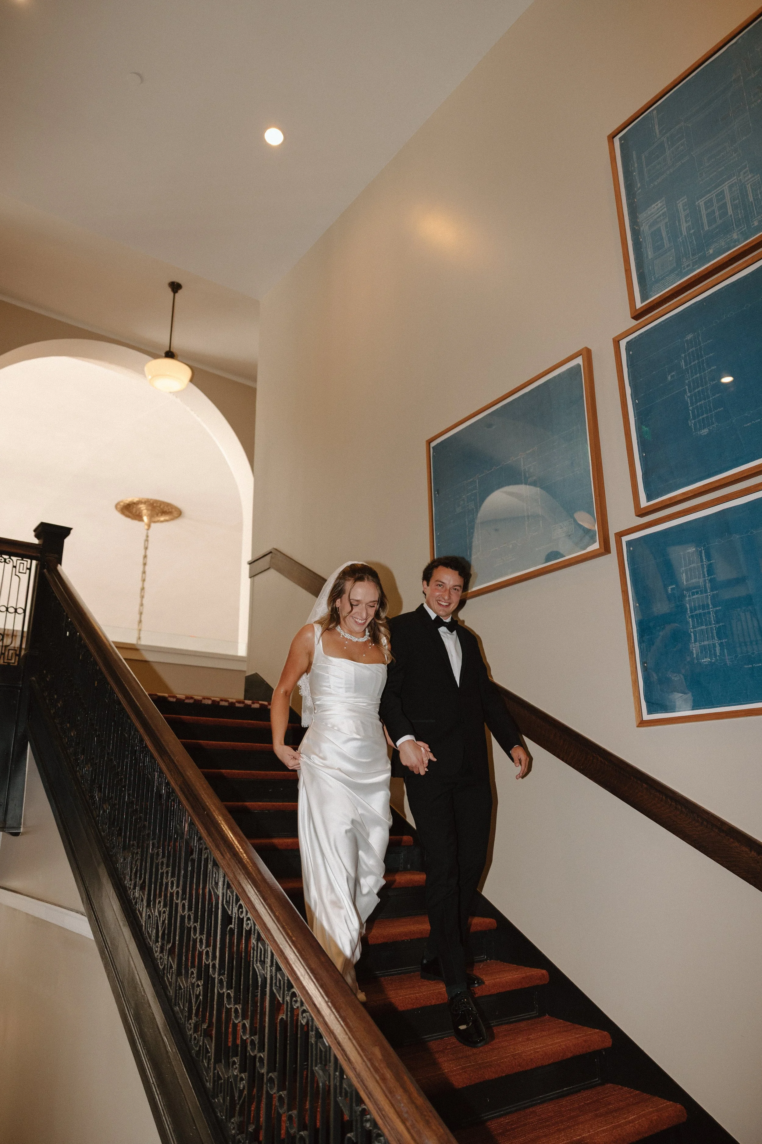 A bride and groom are descending a staircase during their wedding, smiling and holding hands.