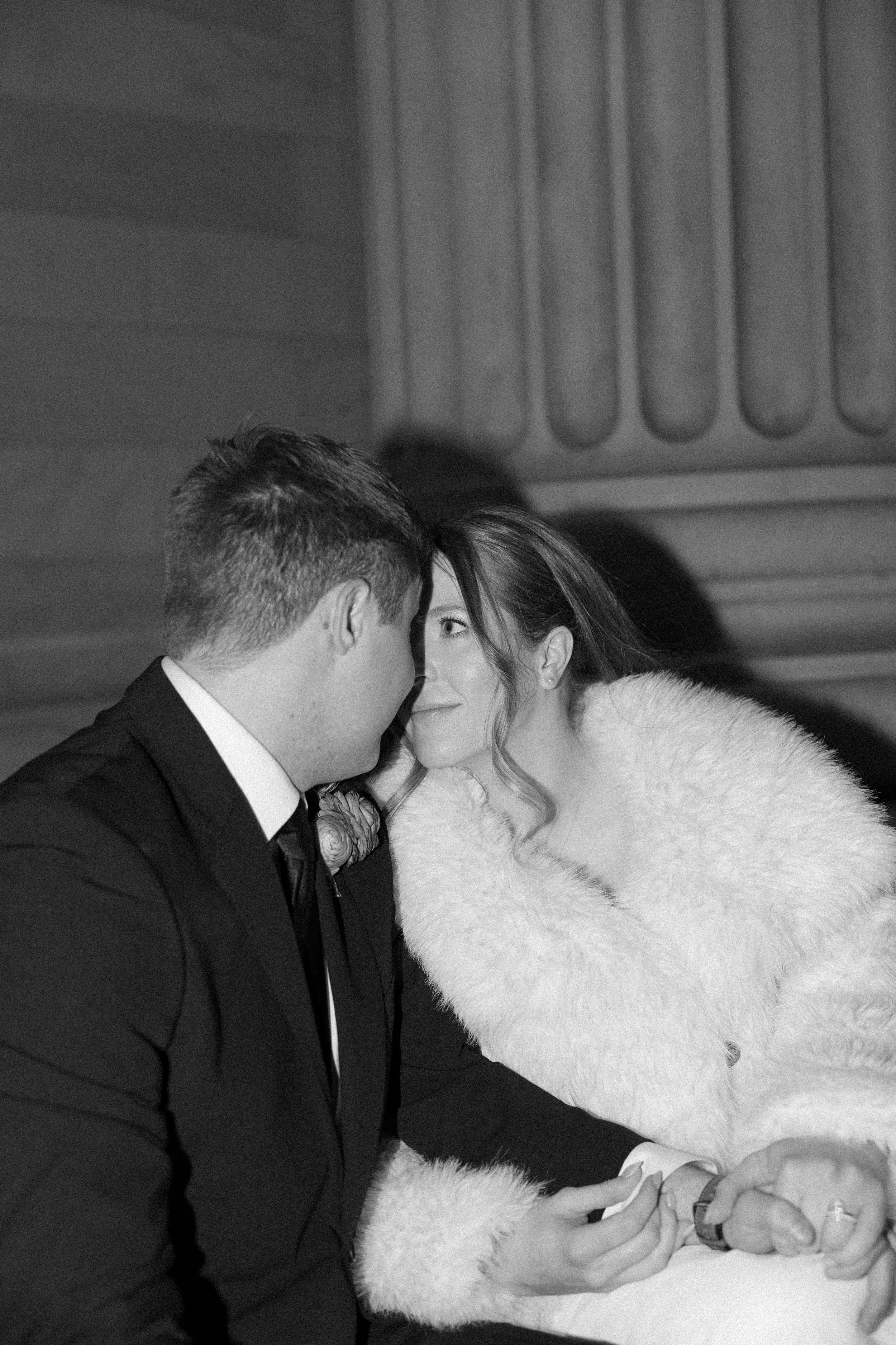 A black and white photo of a romantic moment between a man and a woman, with their foreheads touching and eyes looking at each other, in an intimate setting.