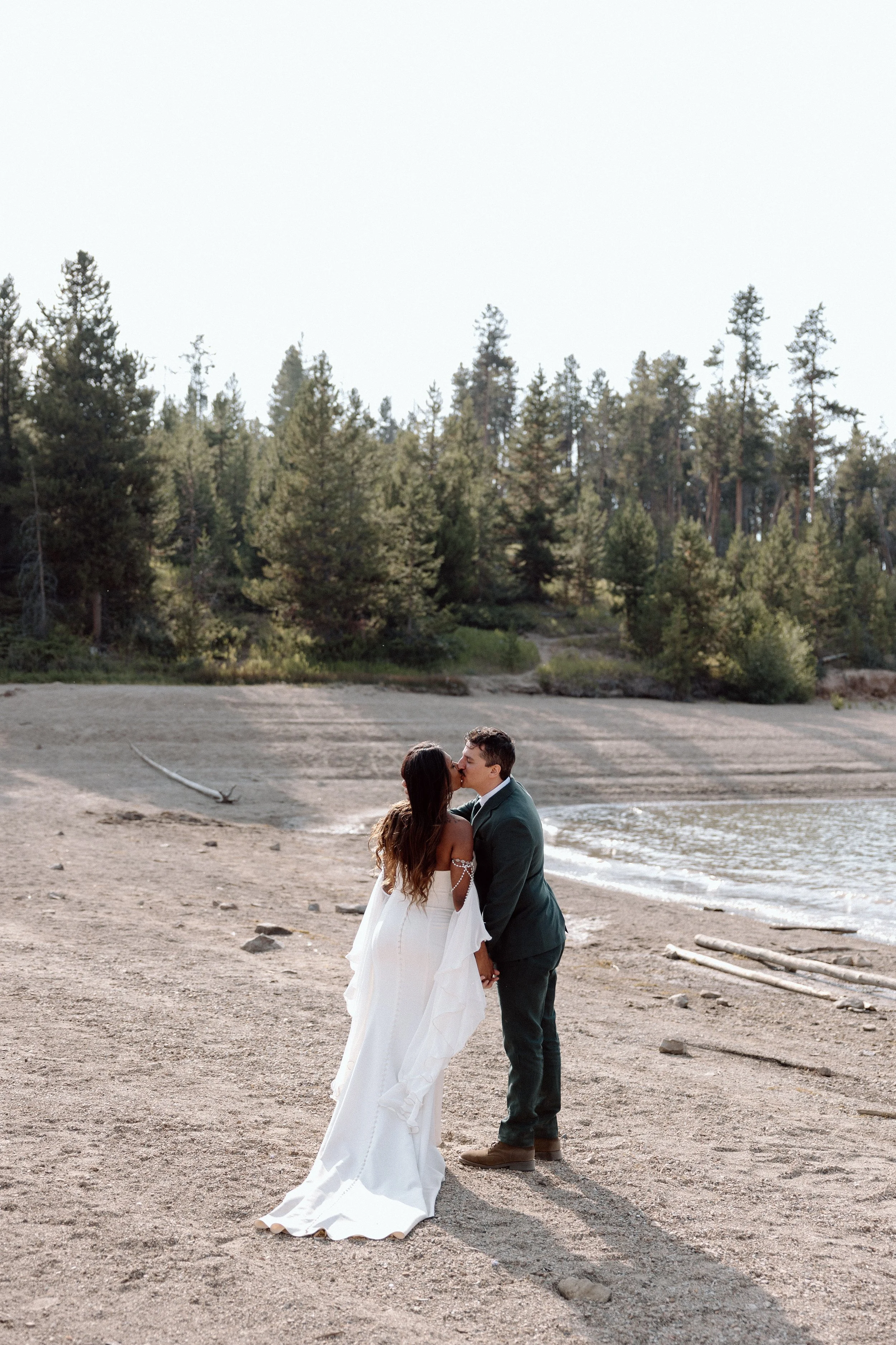 A couple kissing on a sandy beach with trees in the background