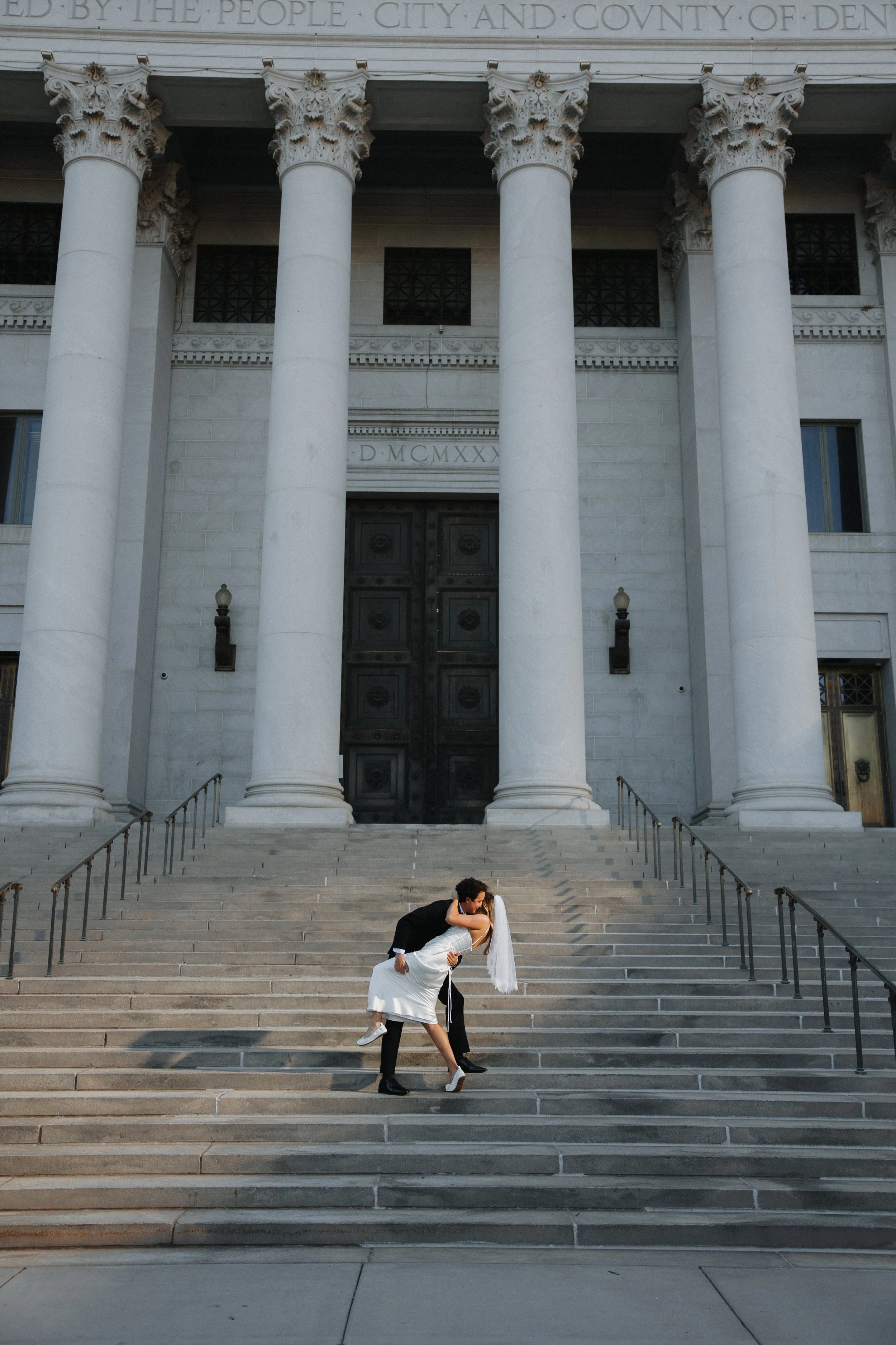 A bride and groom kissing on the steps of a large, historic building with tall columns and ornate architecture.