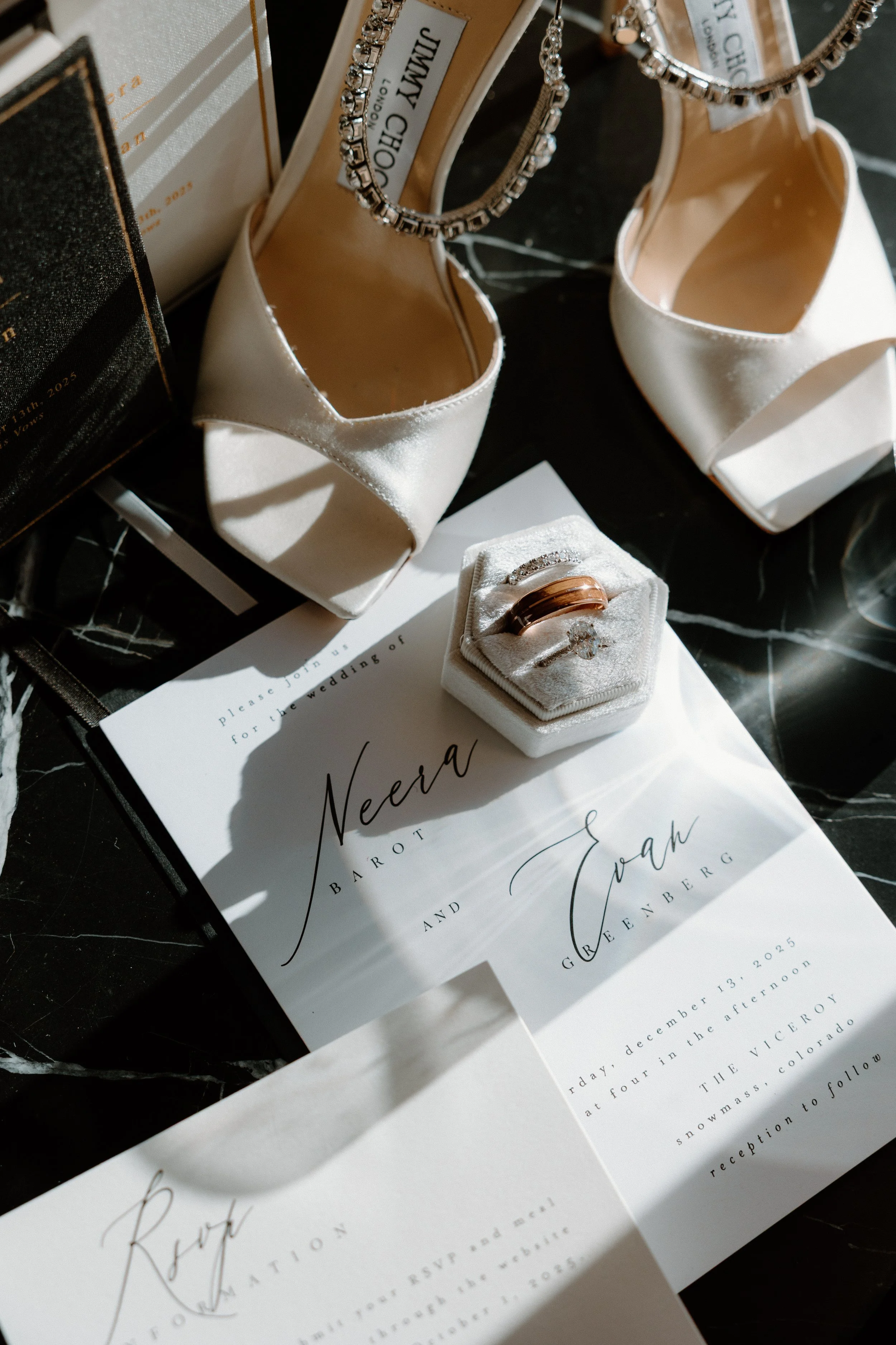 Wedding invitation with rings, white high-heeled shoes with rhinestone ankle straps, and event details.