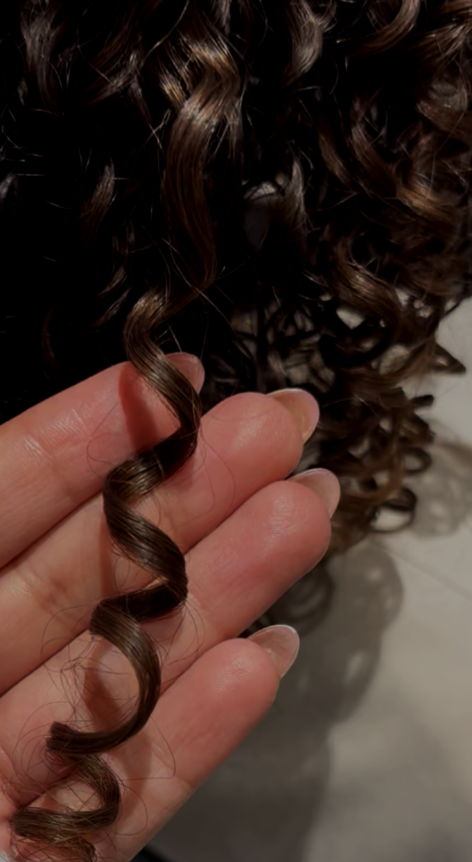 Close-up of 3B curly brown hair strand held between fingers.