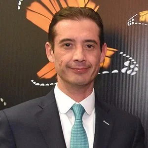 Arq. Manuel Nocetti Villicaña, Tesorero de Onexpo Nacional.
Hombre con cabello peinado hacia atrás, usando un traje oscuro y una corbata azul, sonriendo frente a un fondo con mariposas y formas abstractas de colores brillantes.