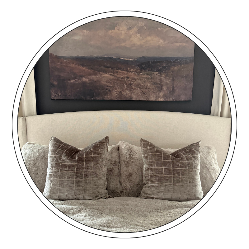 Interior of a bedroom with a beige headboard, plush pillows, and a landscape painting on a dark wall.