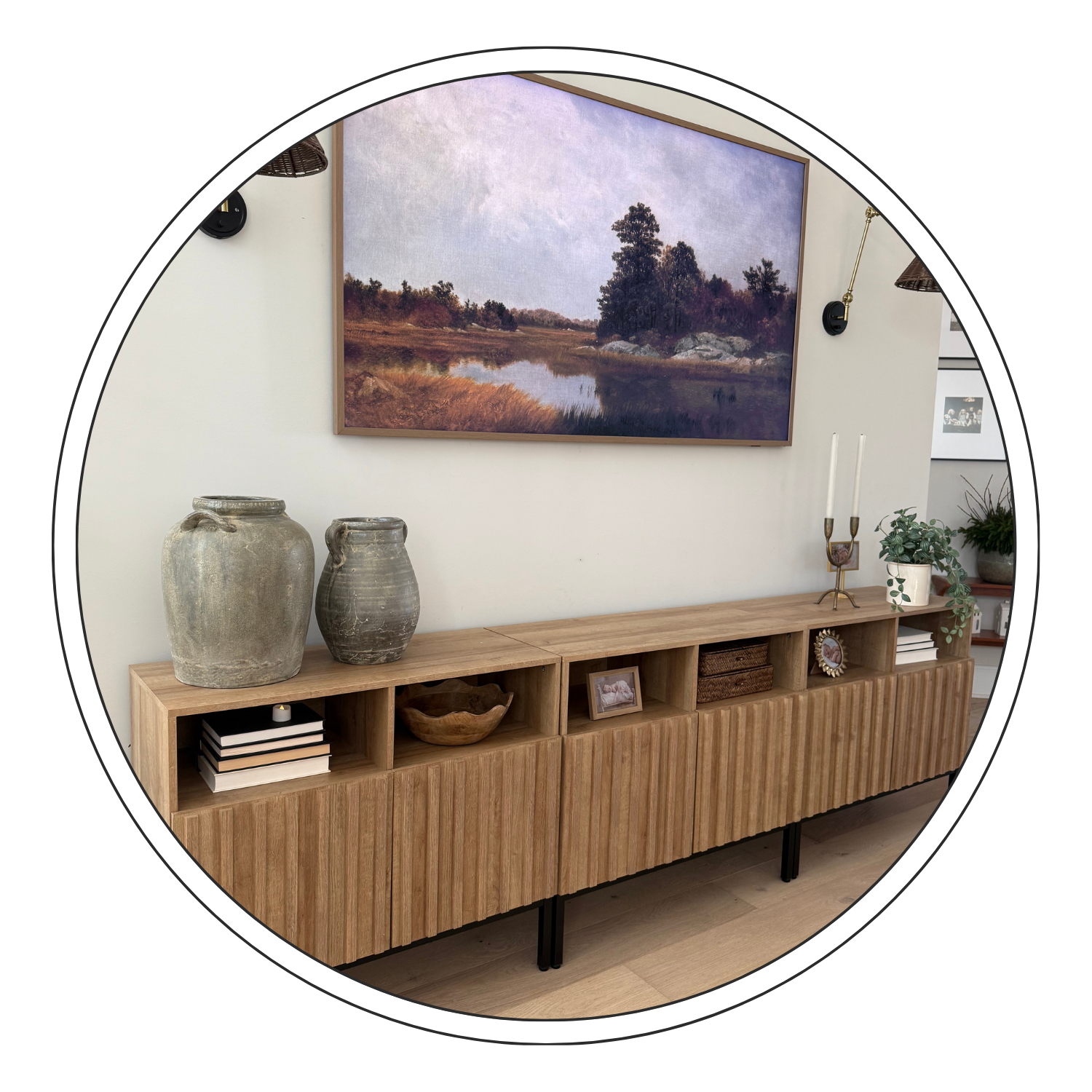 A modern wooden sideboard decorated with vases, a picture frame, a wooden bowl, and candlesticks, with a landscape painting hanging above it on a white wall.