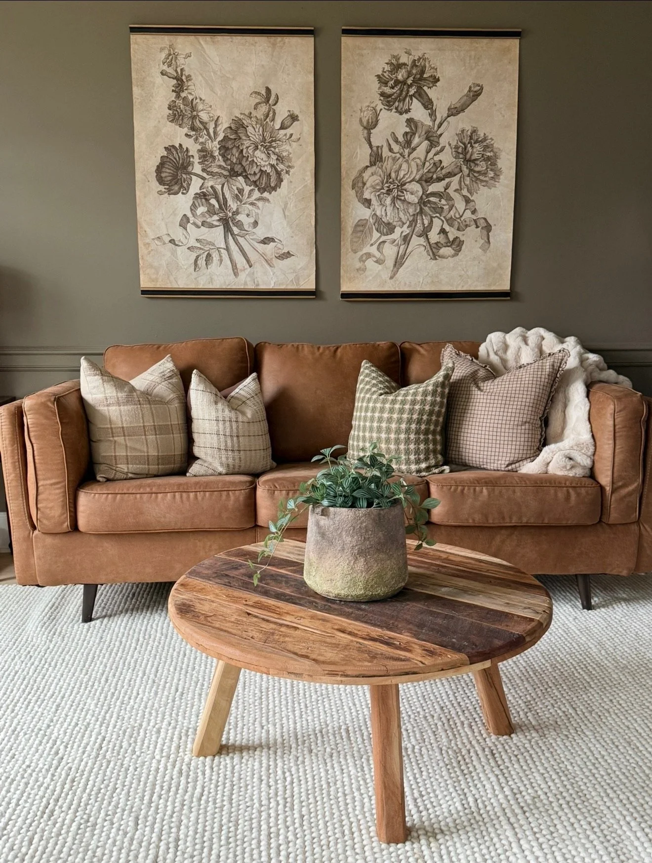 Living room corner with a tan sofa, decorative pillow, and throw blanket, wall art, and a floor lamp with a beige shade.