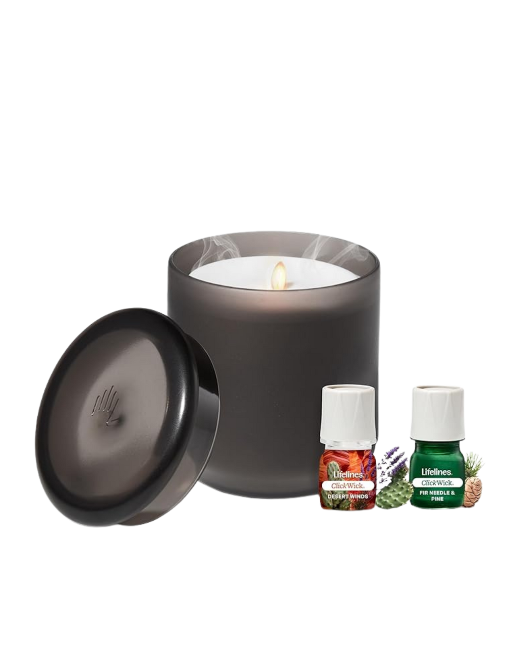 A black candle with a lit white wax interior, with two small bottles of essential oils labeled 'Desert Winds' and 'Fir Needle & Pine', surrounded by sprigs of lavender, pine, and other herbs.