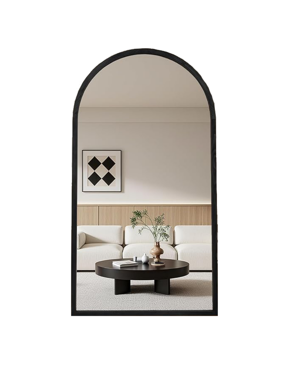 Living room with a beige sofa, black coffee table, decorative plants, and wall art, reflected in an arched mirror.
