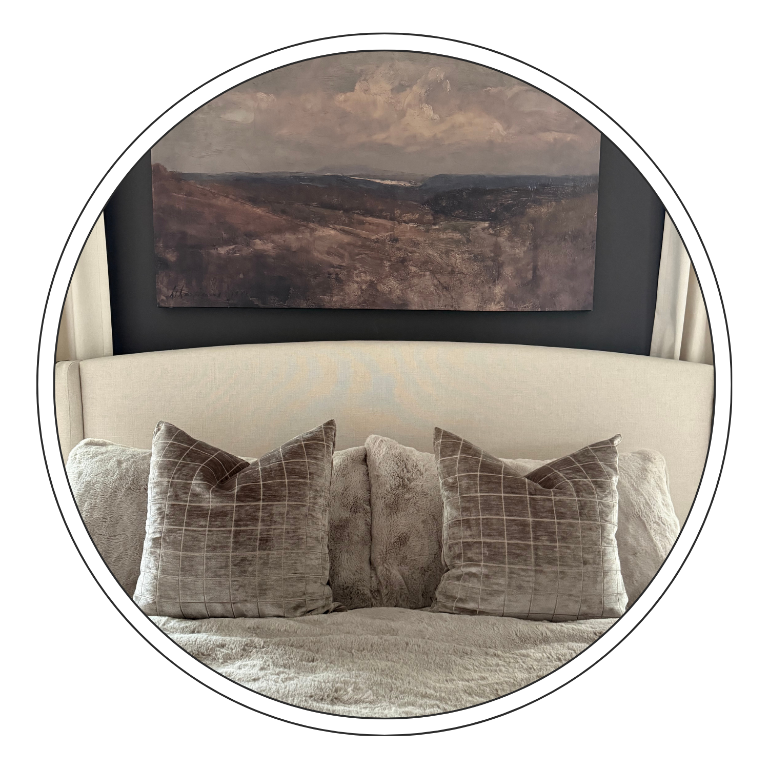 Interior scene with a beige sofa, four plaid cushions, a textured throw, a large landscape painting on a dark wall, and white curtains on either side.