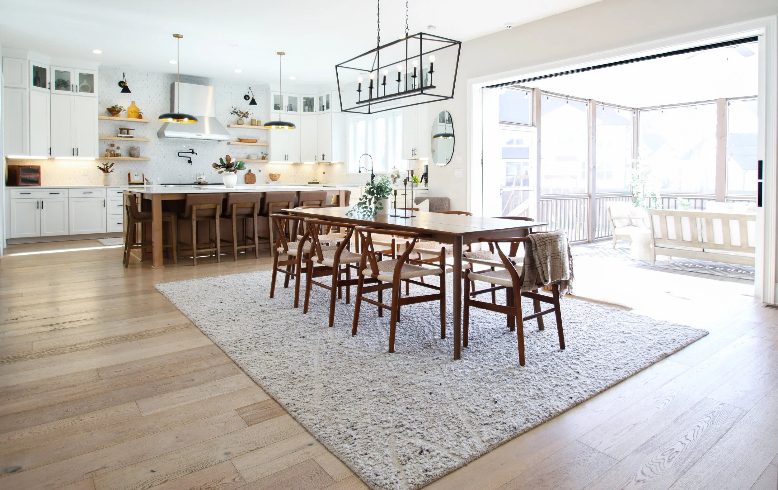 Bright, modern kitchen and dining area with wooden furniture, white cabinets, and sliding glass doors leading to an outdoor patio.