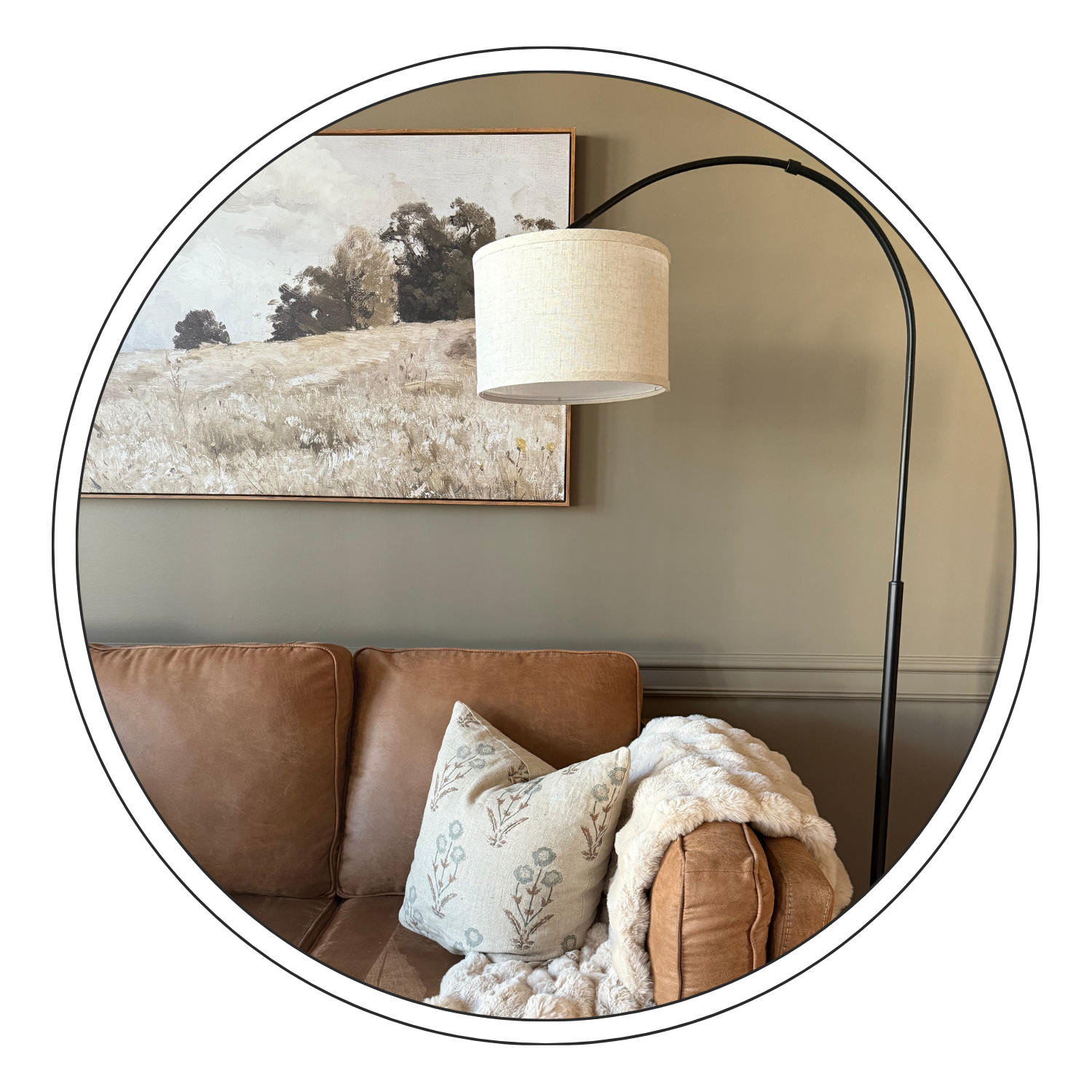 Living room corner with a tan sofa, decorative pillow, and throw blanket, wall art, and a floor lamp with a beige shade.