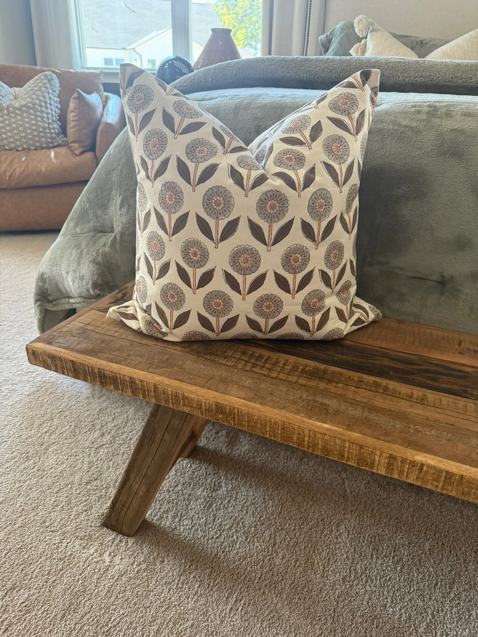 Decorative pillow with floral pattern on a wooden bench near a sofa in a living room.