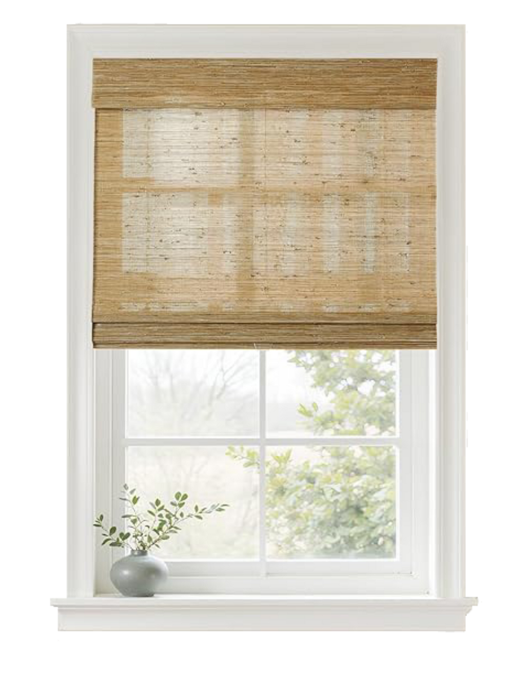 A window with a beige woven roller shade partially lowered, and a small gray vase with greenery on the windowsill. Outside, tree branches and leaves are visible through the window.