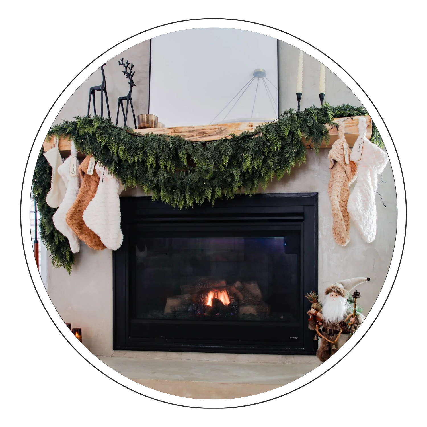 Christmas fireplace mantel decorated with evergreen garland and stockings, with a lit fireplace and festive figurine nearby.