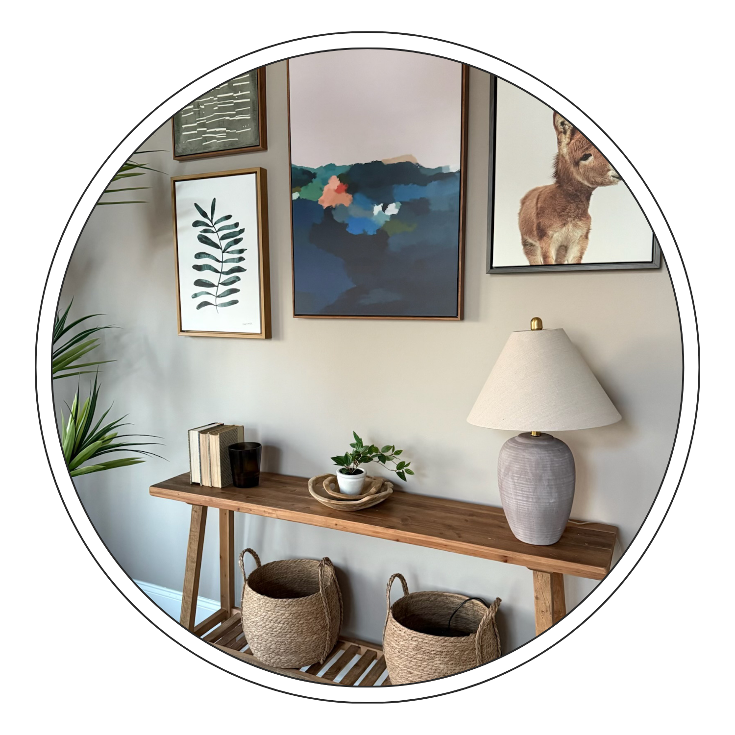 Decorative living room wall with framed artwork, a wooden console table with books, a plant, a tray, and a lamp, flanked by woven baskets.