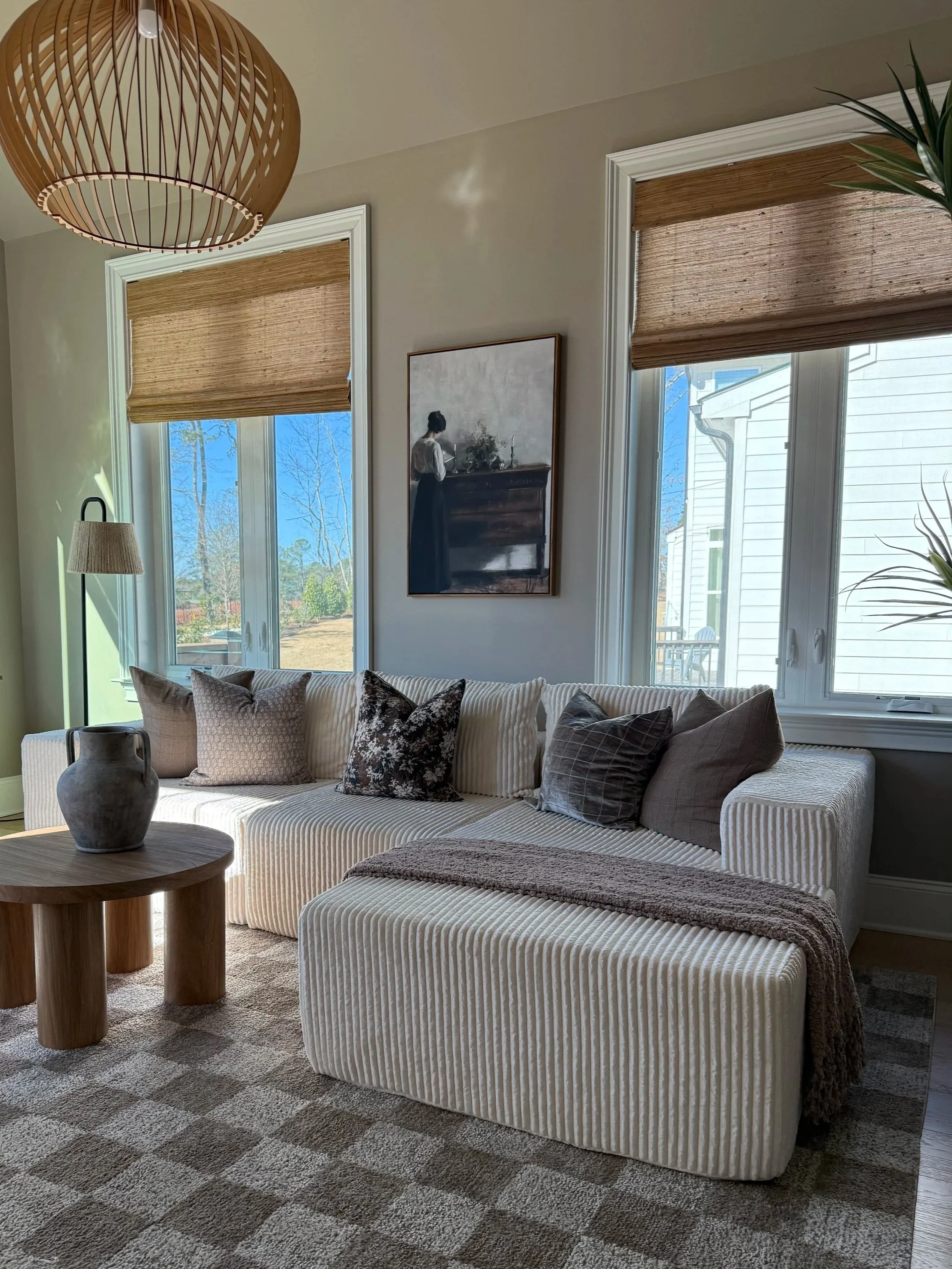 Decorative living room wall with framed artwork, a wooden console table with books, a plant, a tray, and a lamp, flanked by woven baskets.