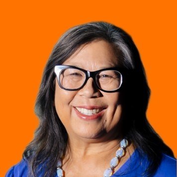 A woman smiling, wearing glasses and a blue top, with an orange background.