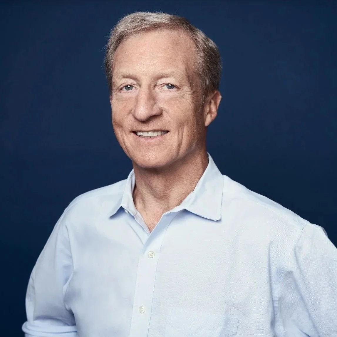 Portrait of a middle-aged man with light brown hair wearing a light blue collared shirt against a dark blue background.