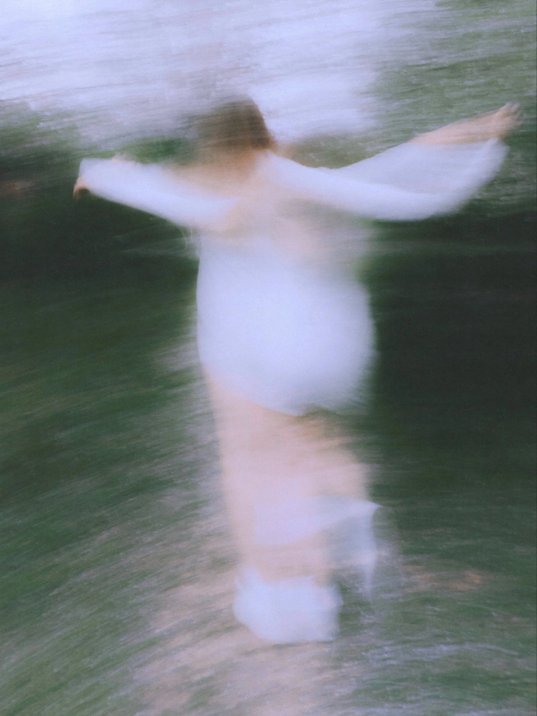 A person swimming in the water with a white shirt or swimsuit, captured with motion blur.