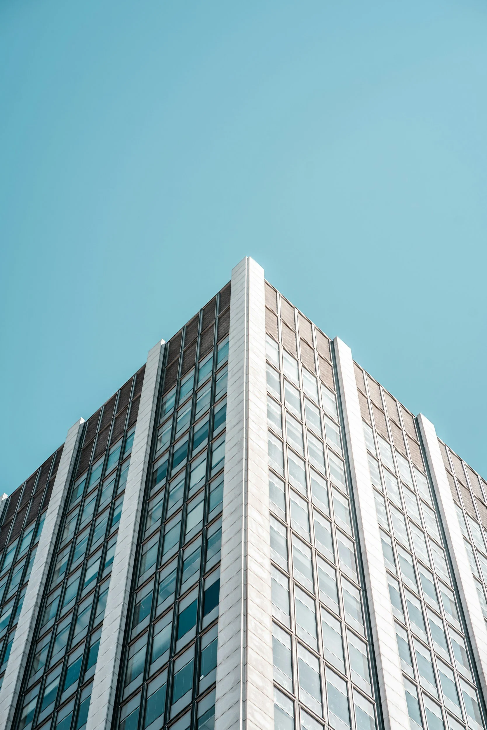 A tall, modern glass office building with a sharp corner, set against a clear blue sky.