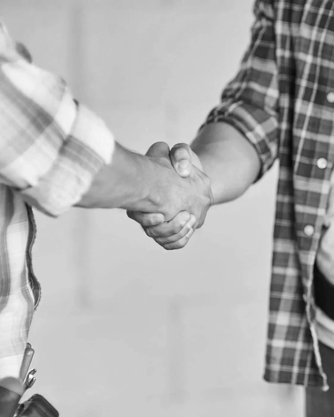 Two people shaking hands, one wearing a plaid shirt with rolled-up sleeves, the other wearing a checkered jacket with a pen in the pocket.