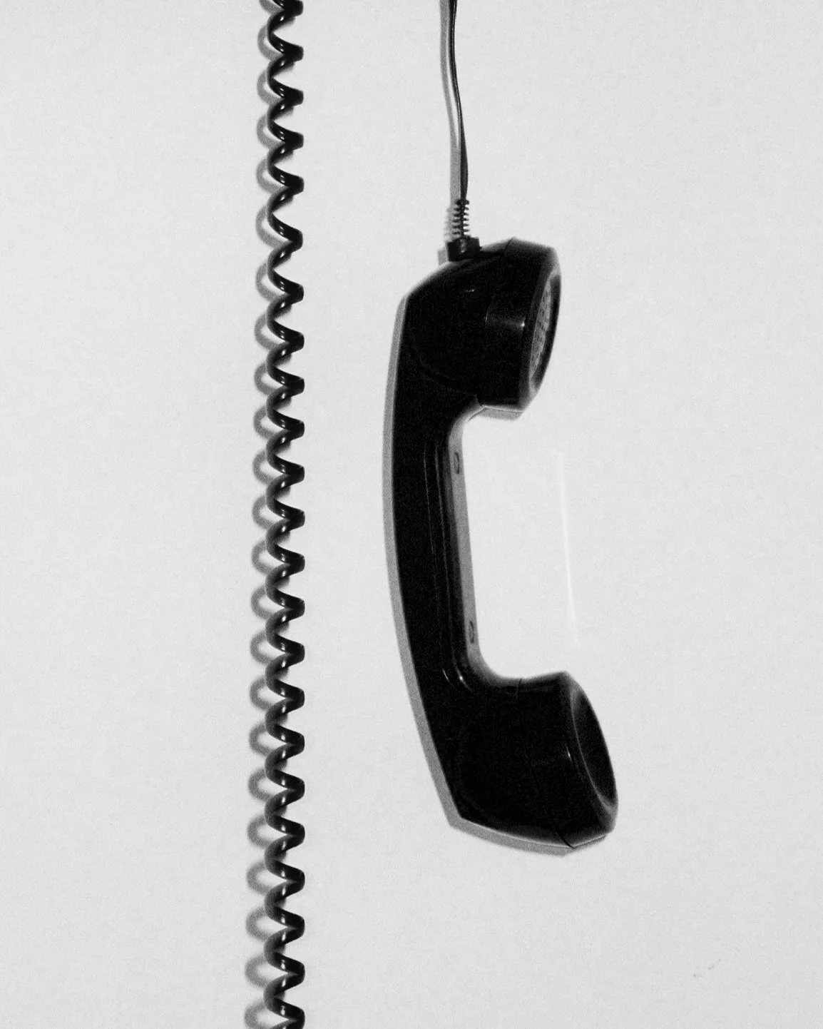 Black corded telephone handset hanging on a wall.