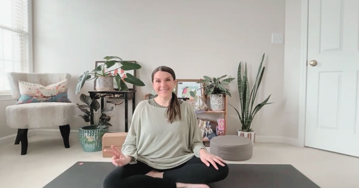 Mel Rolfes seated in an easy pose on a yoga mat in a calm home practice space, representing gentle, grounded online yoga focused on nervous system support.