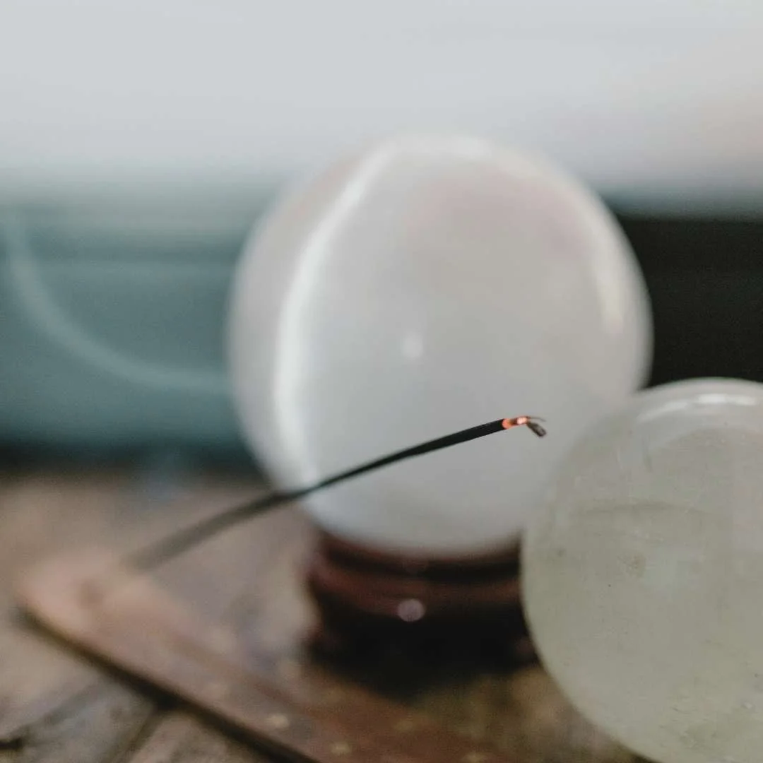 Lit incense resting in a wooden holder beside round crystals, representing the calming, reflective environment of Integrative Guidance sessions with Mel Rolfes.