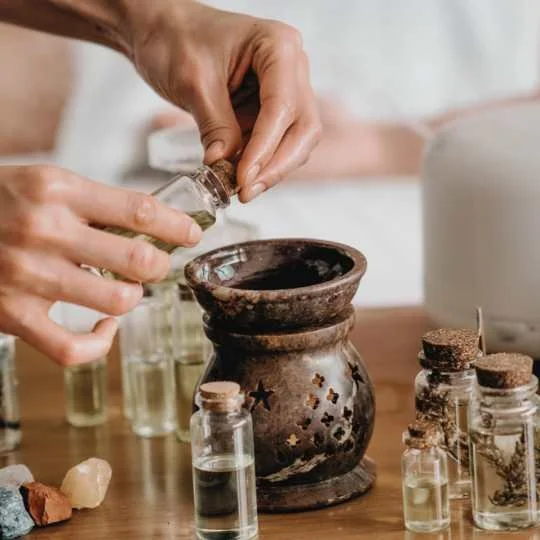 Hands adding herbal oil to a small burner as part of an Ayurvedic self-care or sensory ritual practice