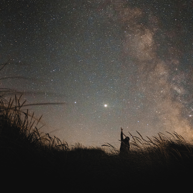 Person standing beneath the Milky Way night sky, reflecting humanity's relationship with the stars and celestial cycles.
