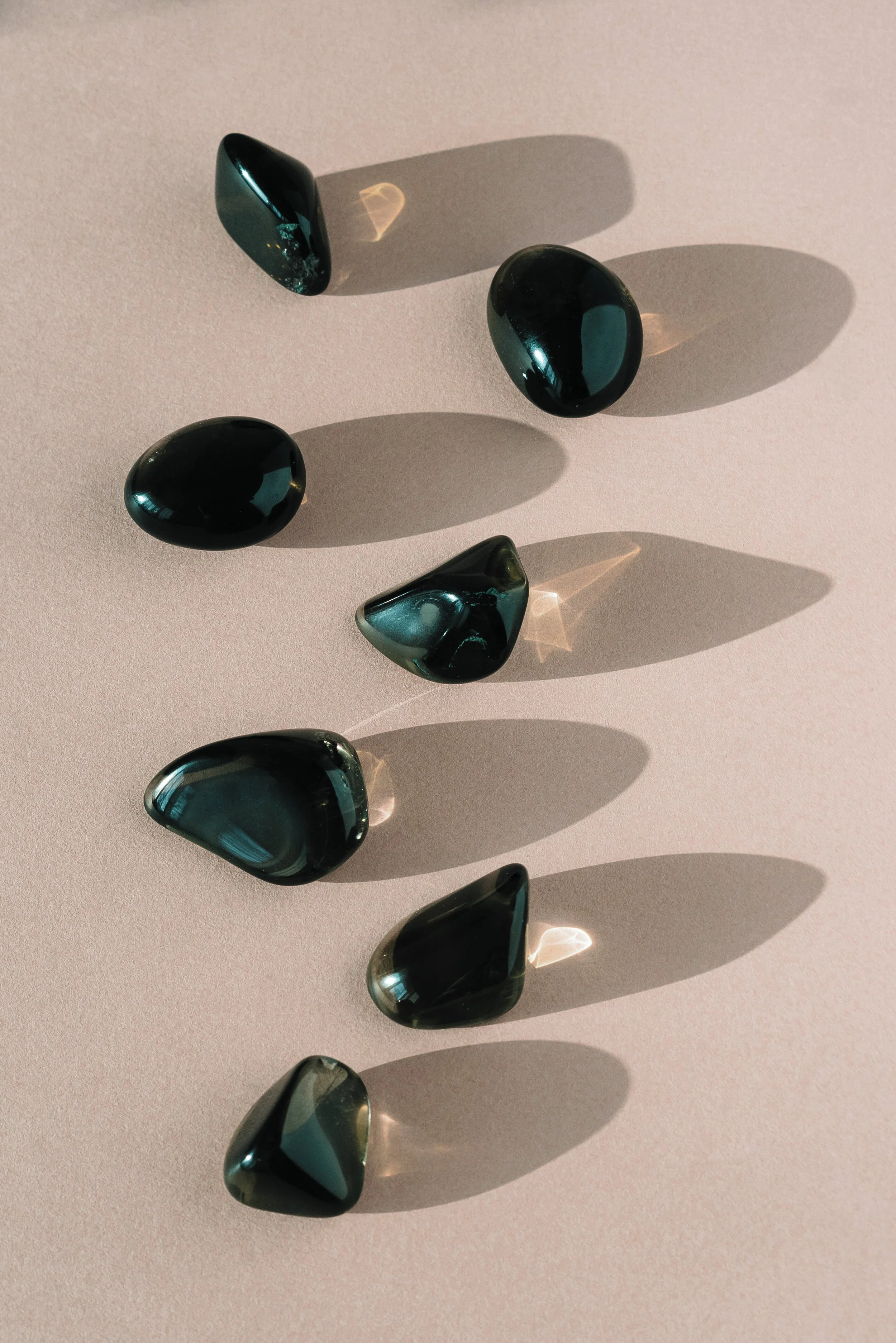 Dark polished stones arranged in soft natural light, used as a grounding visual on the Mel Rolfes integrative guidance, yoga, and 5-Needle Protocol contact page.