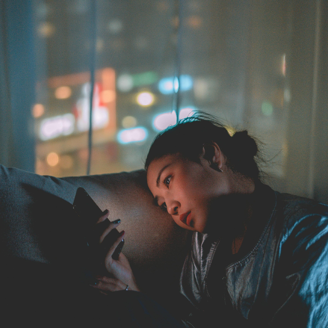 Person sitting alone at night looking at a smartphone, illustrating digital overstimulation, loneliness, and modern disconnection.