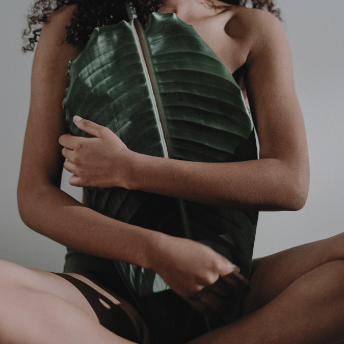 Person holding a large green leaf against their body, symbolizing embodiment, self-awareness, and connection to the natural world.