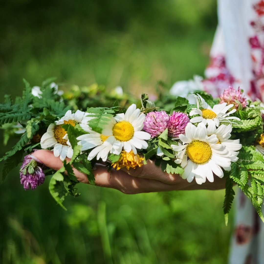 Hand holding a flower crown made from fresh summer blooms, reflecting traditional midsummer celebrations and seasonal observances.